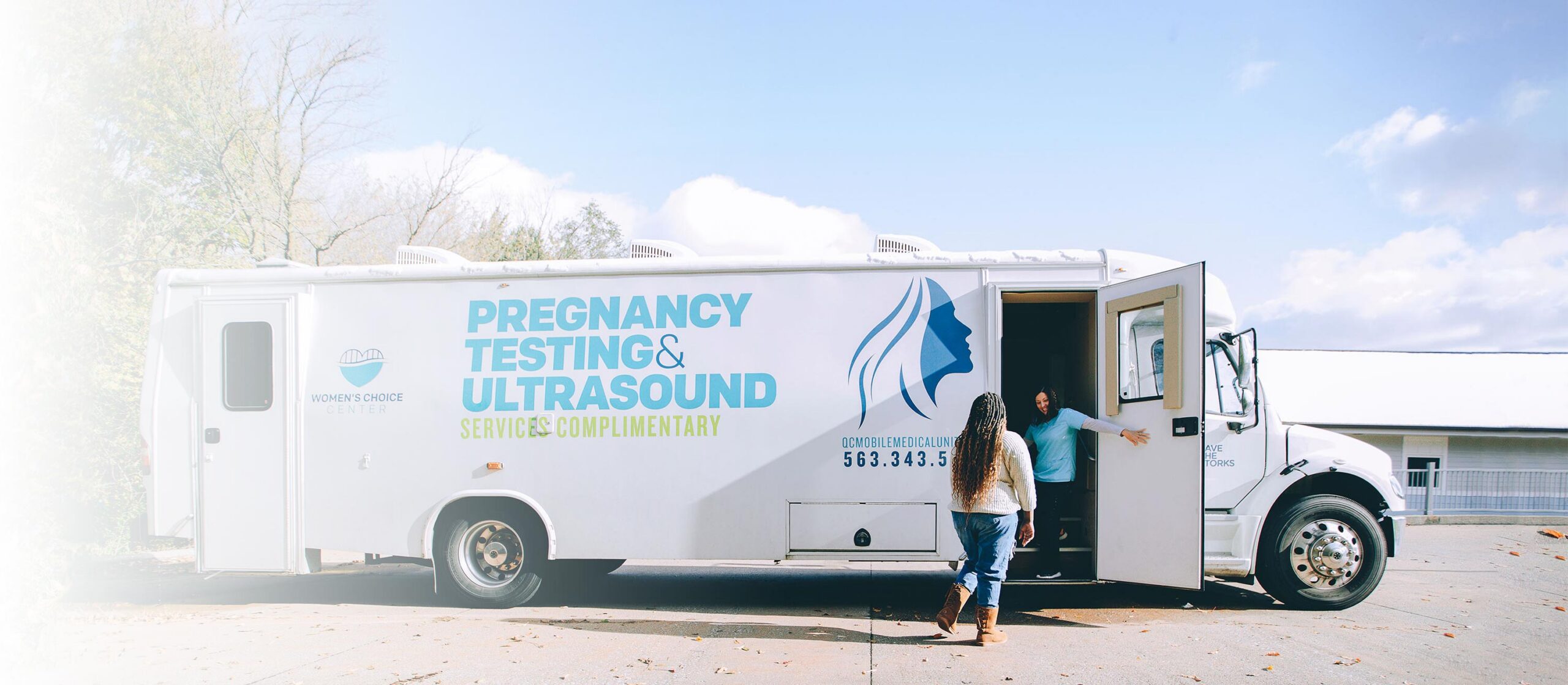 woman opening door of pregnancy testing and ultrasound bus to invite other woman inside.